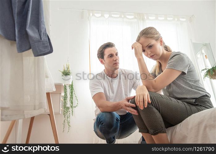 Caucasian young man comforting to the sad unhappy depressed woman sitting on bed in bedroom,finance fail and concerned concept.