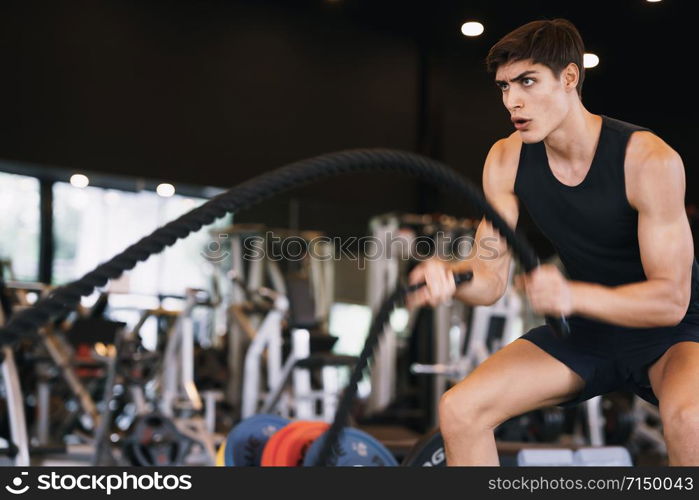 Caucasian young man doing exercises with battle rope strength and motivation in the gym, fitness