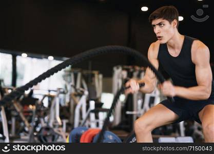Caucasian young man doing exercises with battle rope strength and motivation in the gym, fitness