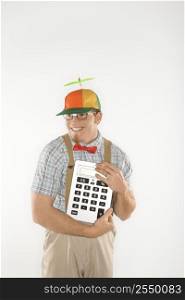 Caucasian young man dressed like nerd wearing beanie and smiling while holding large calculator.