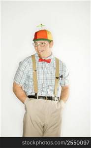 Caucasian young man dressed like nerd wearing propeller cap with hands in pockets.