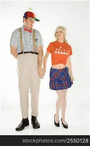 Caucasian young man dressed like nerd wearing propeller hat holding hands with Caucasian blonde young woman wearing tshirt reading I love nerds and plaid skirt.