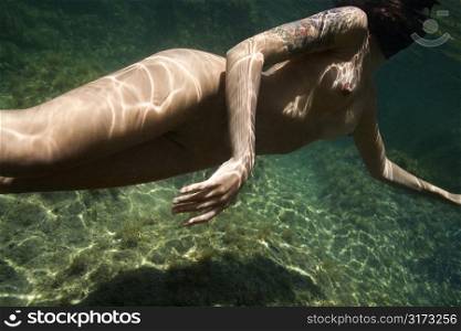 Caucasian young nude female body swimming underwater.