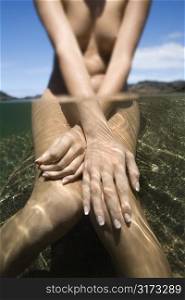 Caucasian young nude female partially submerged in water sitting on rock.