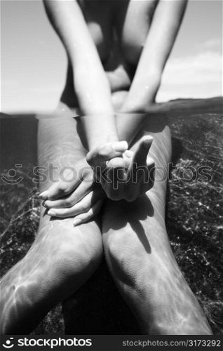 Caucasian young nude female partially submerged in water sitting on rock giving obscene gesture.