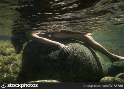 Caucasian young nude woman partially submerged underwater lying on back on rock.