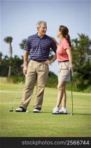 Caucasion mid-adult man and woman standing on golf course talking to each other.