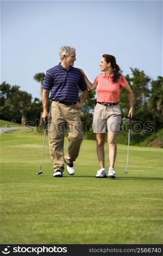 Caucasion mid-adult man and woman walking on golf course talking to each other.
