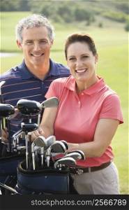 Caucasion mid-adult man and woman with golf clubs smiling and looking at viewer.