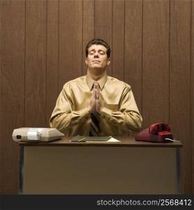 Caucasion mid-adult retro businessman sitting at desk praying in gratitude.