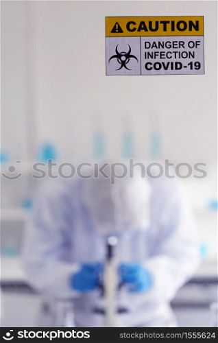 Caution danger Signage of COVID-19 coronavirus in front of Laboratory room with background of Scientists working and researching vaccine for ncov-19 virus for world pandemic situation.