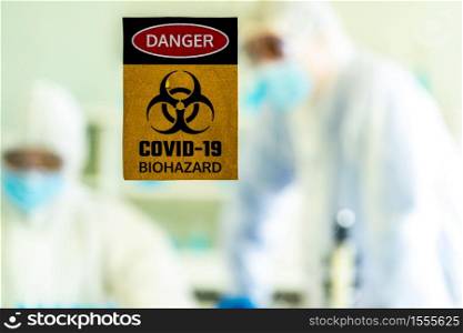 Caution danger Signage of COVID-19 coronavirus in front of Laboratory room with background of Scientists working and researching vaccine for ncov-19 virus for world pandemic situation.