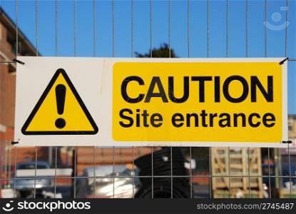 caution site entrance sign hanging on a metallic fence at a construction site