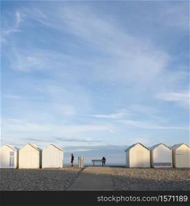 cayeux, france, 6 august 2020: people near beach huts in cayeux s mer in french normandy under blue sky in early morning sunlight