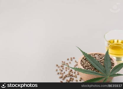 CBD oil, THC tinture in glass bowl and bottle with dropper lid and hemp leaf on empty background with a pile of dry hemp seeds surrounded in minimalism. Legalized marijuana concept.. Legalized marijuana concept CBD oil in glass bowl and bottle with dropper lid.