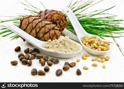 Cedar flour and peeled nuts in two spoons, two cones, a green cedar branch on a wooden board background