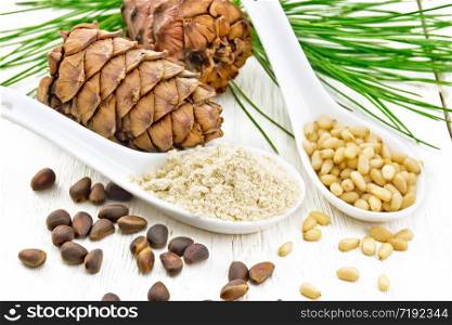 Cedar flour and peeled nuts in two spoons, two cones, a green cedar branch on background of a light wooden board