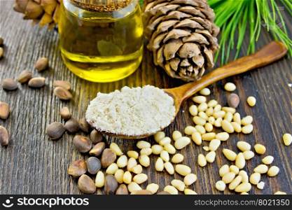 Cedar Flour in a wooden spoon, cedar nuts and two cones, cedar oil in a glass jar, a cedar branch with green needles on the background of wooden boards