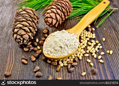Cedar Flour in a wooden spoon, cedar nuts and two cones, green cedar branch on a background of wooden boards