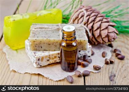 Cedar oil in a bottle, cedar cone, three homemade soap, cedar nuts on the background of wooden boards