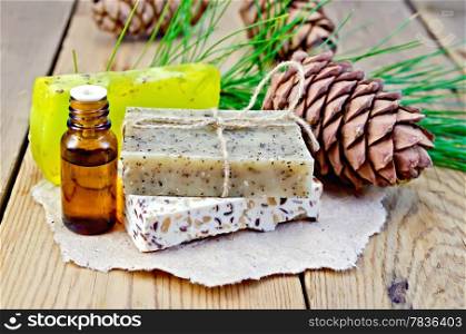 Cedar oil in a bottle, cedar cone, three homemade soap on a paper on the background of wooden boards