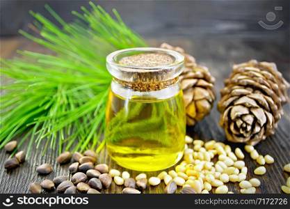 Cedar oil in a glass jar, two cedar cones, nuts and green twigs on a dark wooden board background