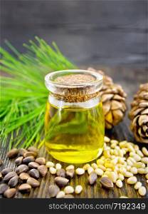 Cedar oil in a glass jar, two cedar cones, nuts and green twigs on a wooden board background