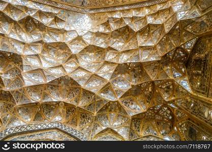 Ceiling texture of decorative golden muqarnas vaulting with mirror work at the entrance of the Chehel Sotoun Palace. Isfahan, Iran.