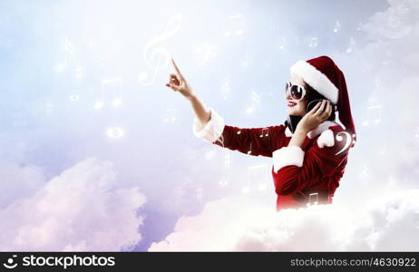 Celebrating New Year. Young attractive Santa girl listening music in headphones