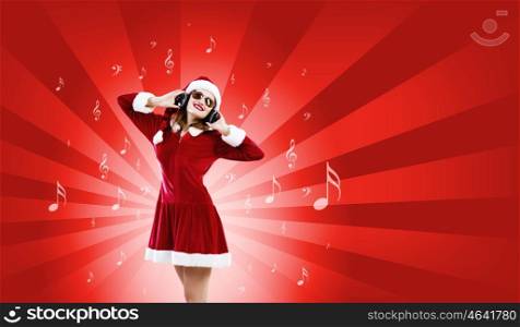 Celebrating New Year. Young attractive Santa girl listening music in headphones