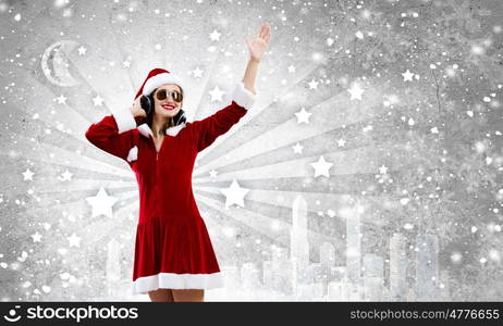 Celebrating New Year. Young attractive Santa girl listening music in headphones