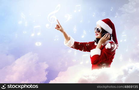 Celebrating New Year. Young attractive Santa girl listening music in headphones