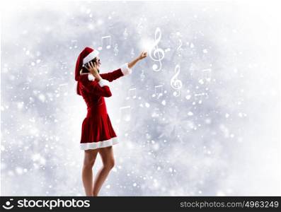 Celebrating New Year. Young attractive Santa girl listening music in headphones