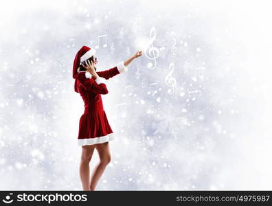 Celebrating New Year. Young attractive Santa girl listening music in headphones