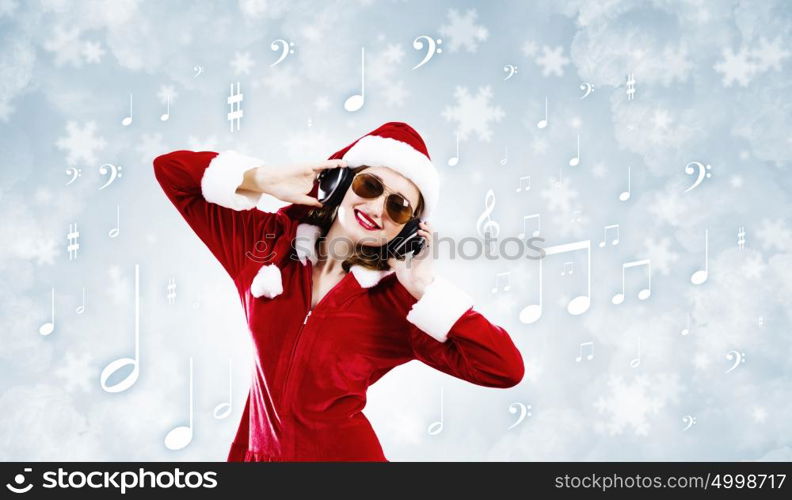 Celebrating New Year. Young attractive Santa girl listening music in headphones