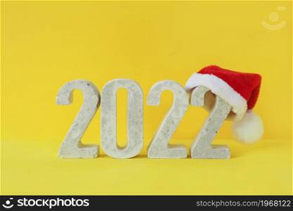 Celebrating the new year 2022. Concrete numeral number 2022 in santa hat on yellow background.