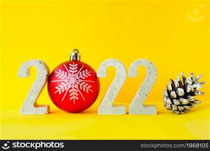 Celebrating the new year 2022. Number 2022 with concrete numbers and a Christmas tree ball on a yellow background with a fir cone.