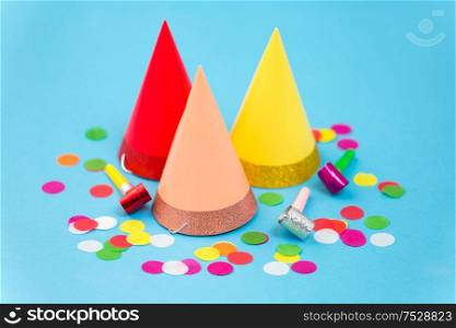 celebration and decoration concept - three birthday party caps, horns and colorful confetti on blue background. birthday party caps, horns and colorful confetti