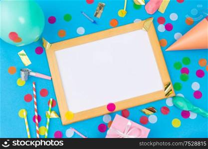 celebration and decoration concept - white board in frame, pink birthday gift, party props, balloons and colorful confetti on blue background. white board, birthday gift and party props