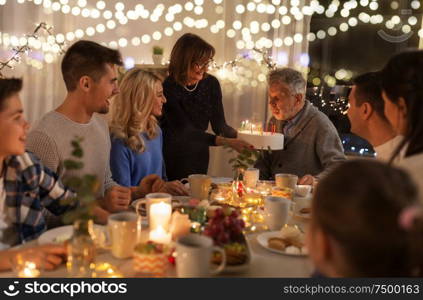 celebration and family concept - happy grandfather blowing candles on birthday cake at dinner party at home. happy family having birthday party at home