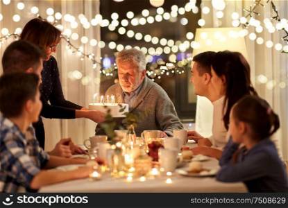 celebration and family concept - happy grandfather blowing candles on birthday cake at dinner party at home. happy family having birthday party at home