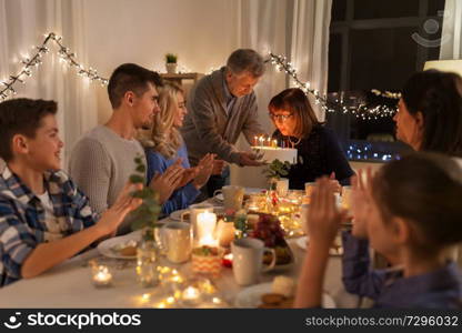 celebration and family concept - happy grandmother blowing candles on birthday cake at dinner party at home. happy family having birthday party at home