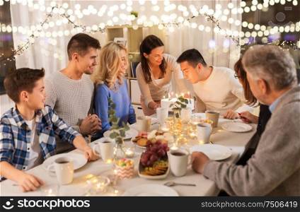 celebration and family concept - happy man blowing candles on birthday cake at dinner party at home. happy family having birthday party at home