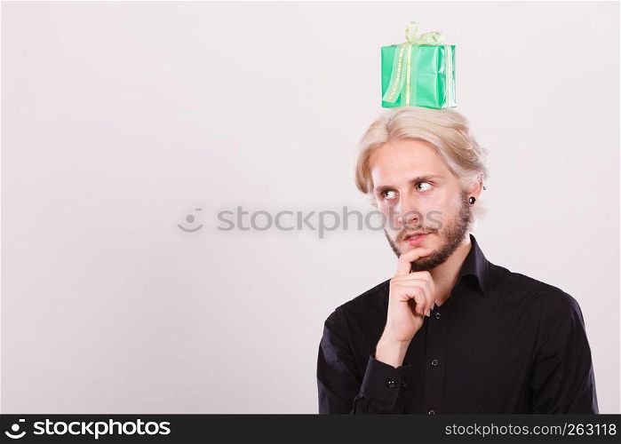 Celebration and giving concept. Cool young man with green gift box on his head. Guy thinking looking for present idea. Thinking guy with green gift box on his head