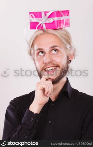 Celebration and giving concept. Cool young man with pink gift box on his head. Guy thinking looking for present idea. Thinking guy with pink gift box on his head