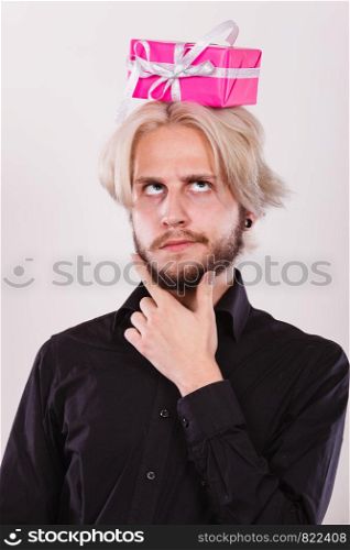 Celebration and giving concept. Cool young man with pink gift box on his head. Guy thinking looking for present idea. Thinking guy with pink gift box on his head