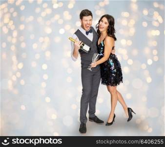 celebration and holidays concept - happy couple with bottle of non alcoholic champagne and wine glasses at party over festive lights background. happy couple with champagne and glasses at party