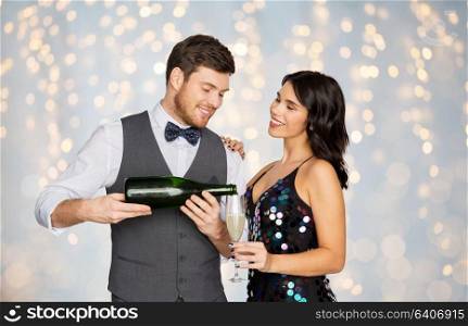 celebration and holidays concept - happy couple with bottle of non alcoholic champagne and wine glass at party over festive lights background. happy couple with champagne and glass at party