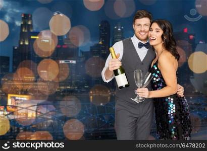celebration and holidays concept - happy couple with bottle of non alcoholic champagne and wine glasses at party over singapore city night lights background. happy couple with champagne and glasses at party. happy couple with champagne and glasses at party