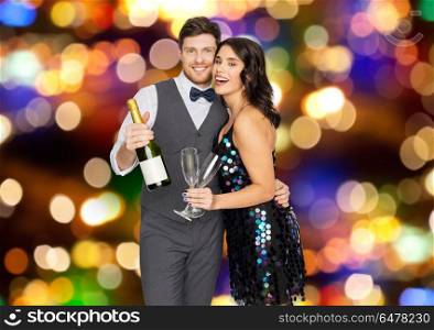 celebration and holidays concept - happy couple with bottle of non alcoholic champagne and wine glasses at party over lights background. happy couple with champagne and glasses at party. happy couple with champagne and glasses at party